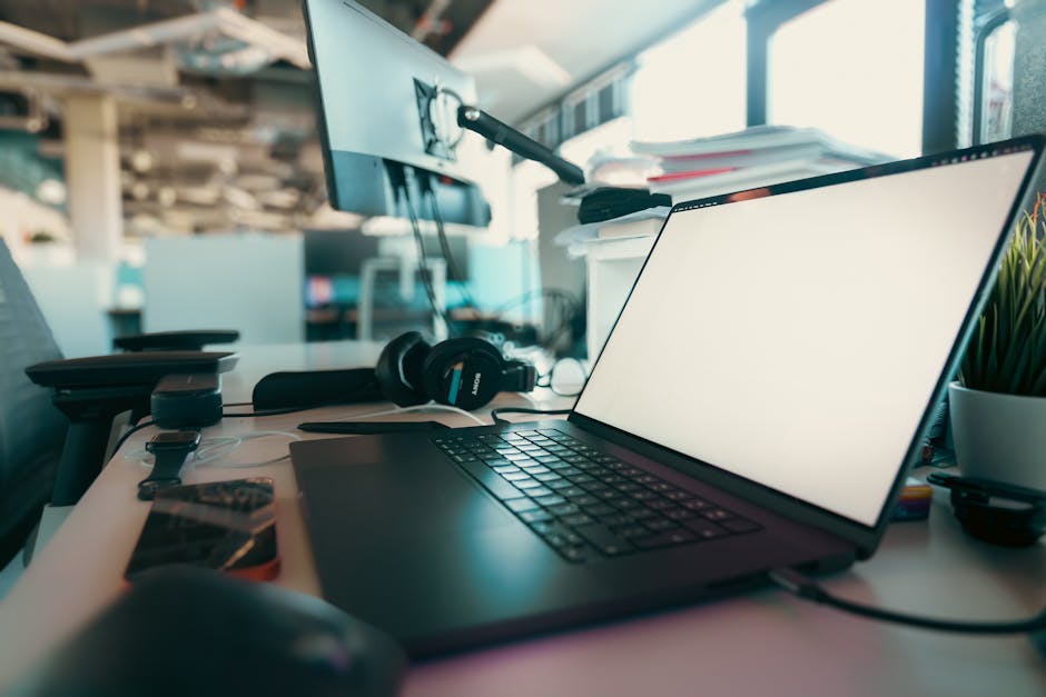 A contemporary office desk setup featuring a laptop, monitor, and headphones
